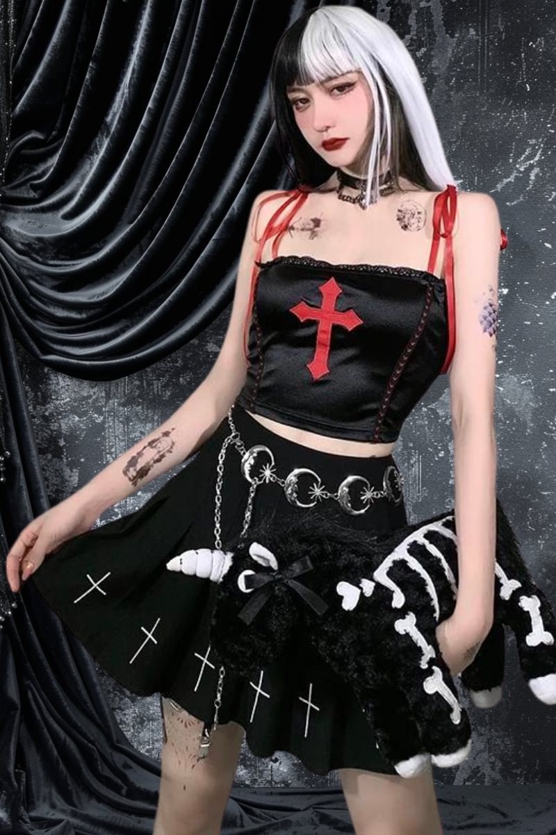 Crop top gothique noir en velours avec croix rouge brodée sur le devant, porté par un mannequin avec jupe noire à motifs ossements blancs et ceinture à anneaux métalliques