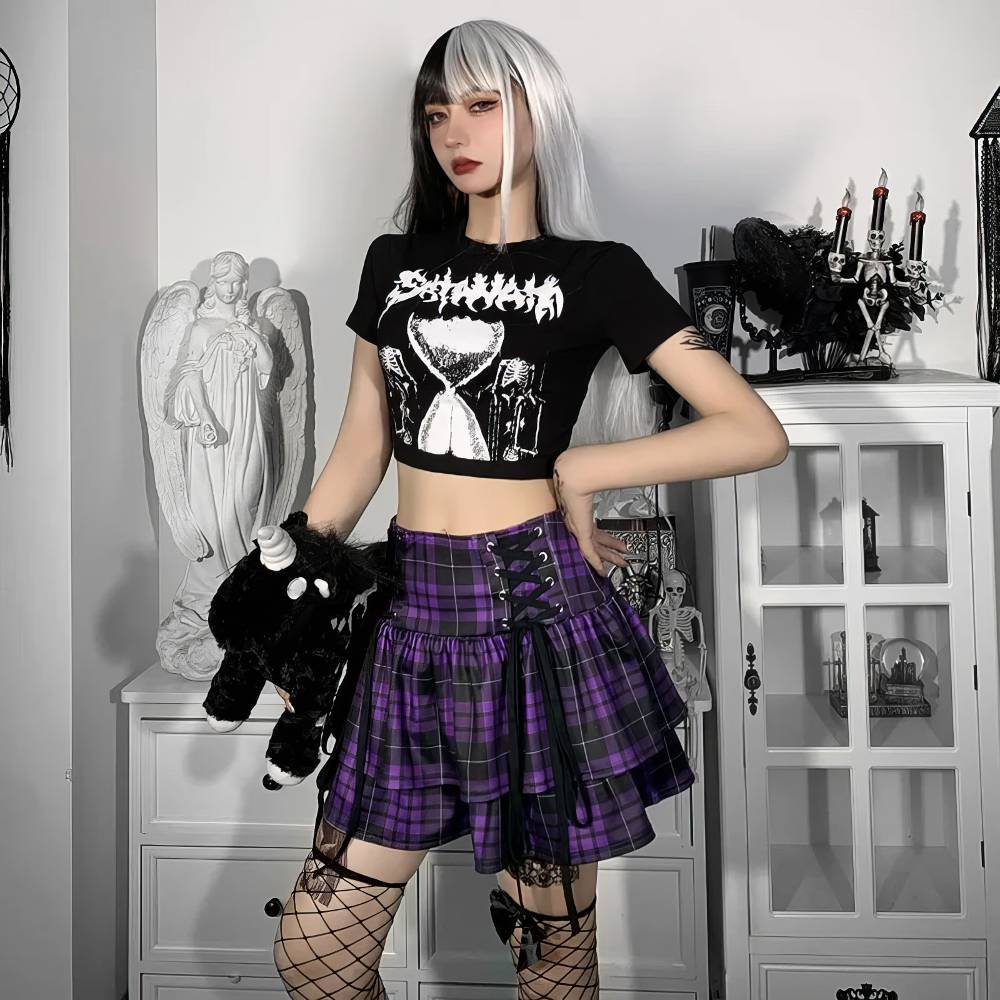 Jupe ecossaise gothique Lunaria en tissu violet à carreaux noirs, plissée avec détails de sangles et boucles métalliques, portée avec un t-shirt noir et bas résille