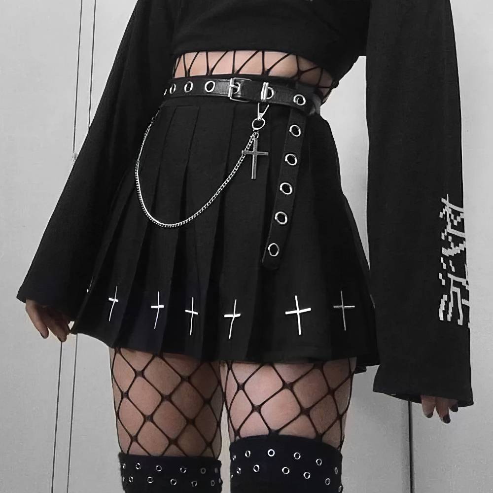 Jupe noire gothique plissée Vortexveinia avec croix blanches brodées en bas, ceinture à œillets et chaîne argentée, portée avec collants résille et haut noir à manches longues