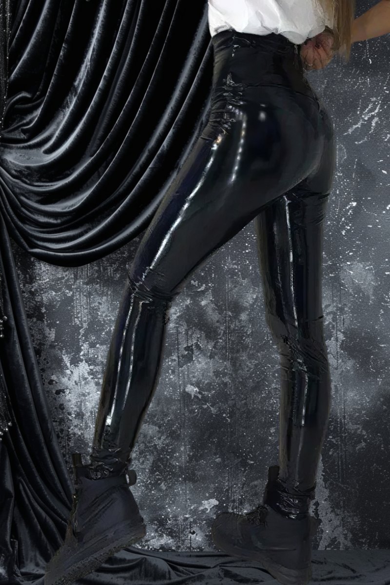 Pantalon cuir gothique noir brillant coupe slim porté de profil avec bottines noires sur fond texturé sombre et drapé velours noir