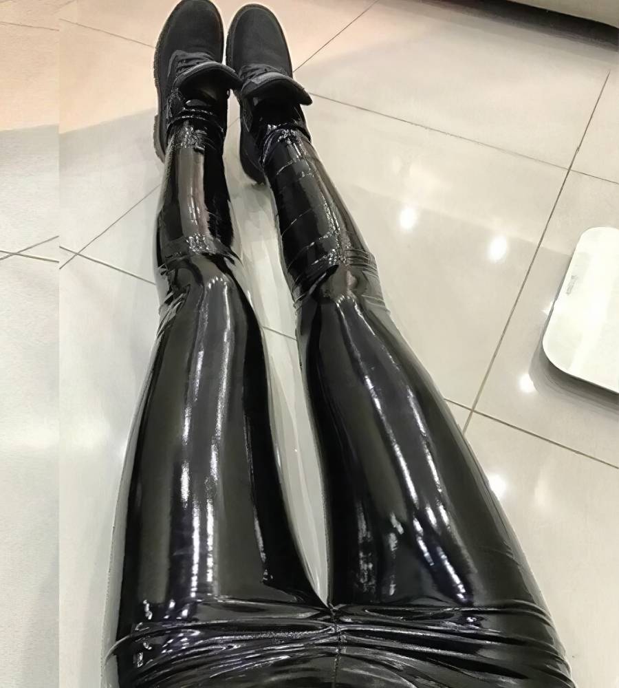 Pantalon cuir gothique noir brillant porté, vue en plongée sur les jambes allongées avec chaussures noires