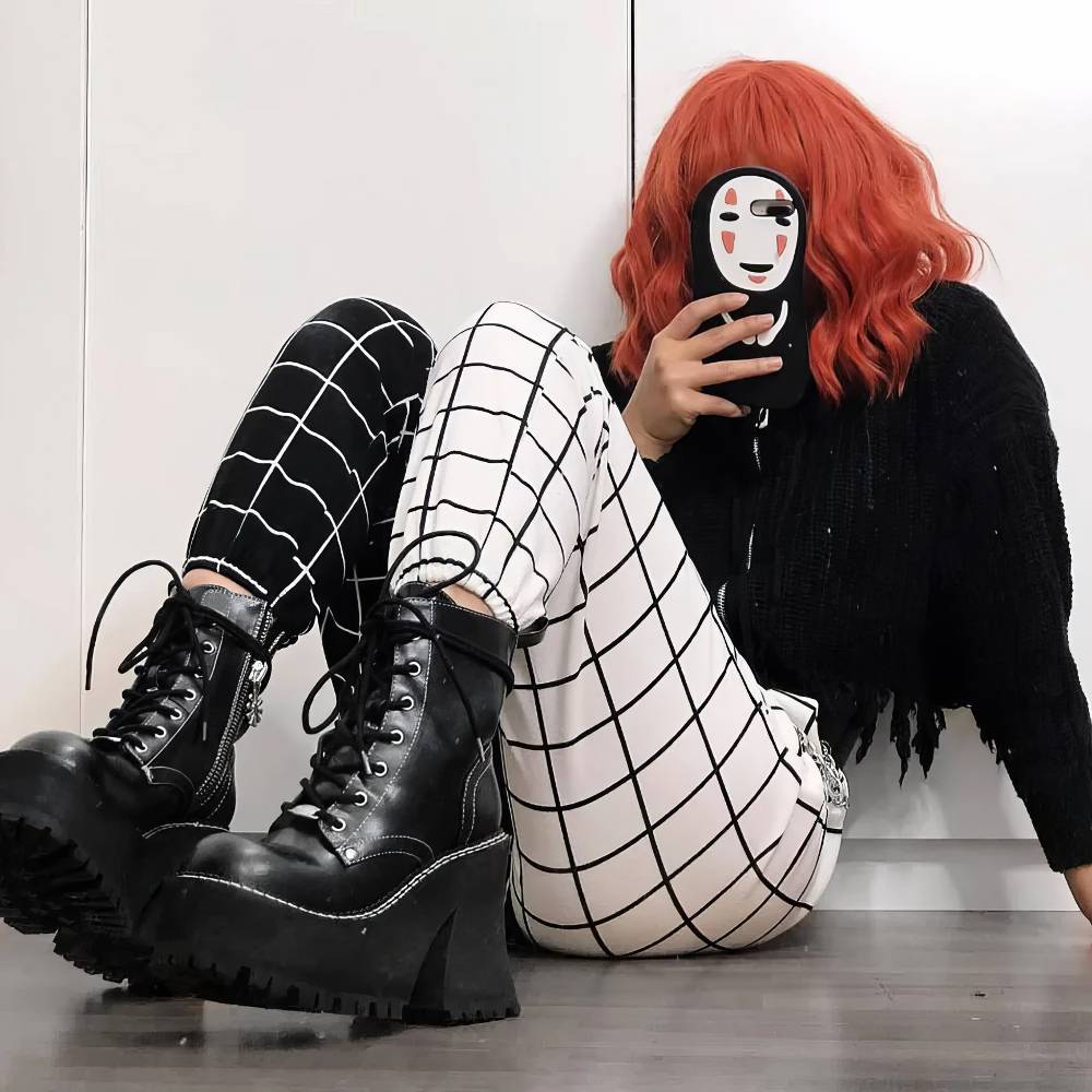 Pantalon gothique femme noir et blanc modèle DarkWhiteWave avec motif quadrillé asymétrique, jambe gauche blanche à carreaux noirs et jambe droite noire à carreaux blancs, porté avec bottines noires à plateforme