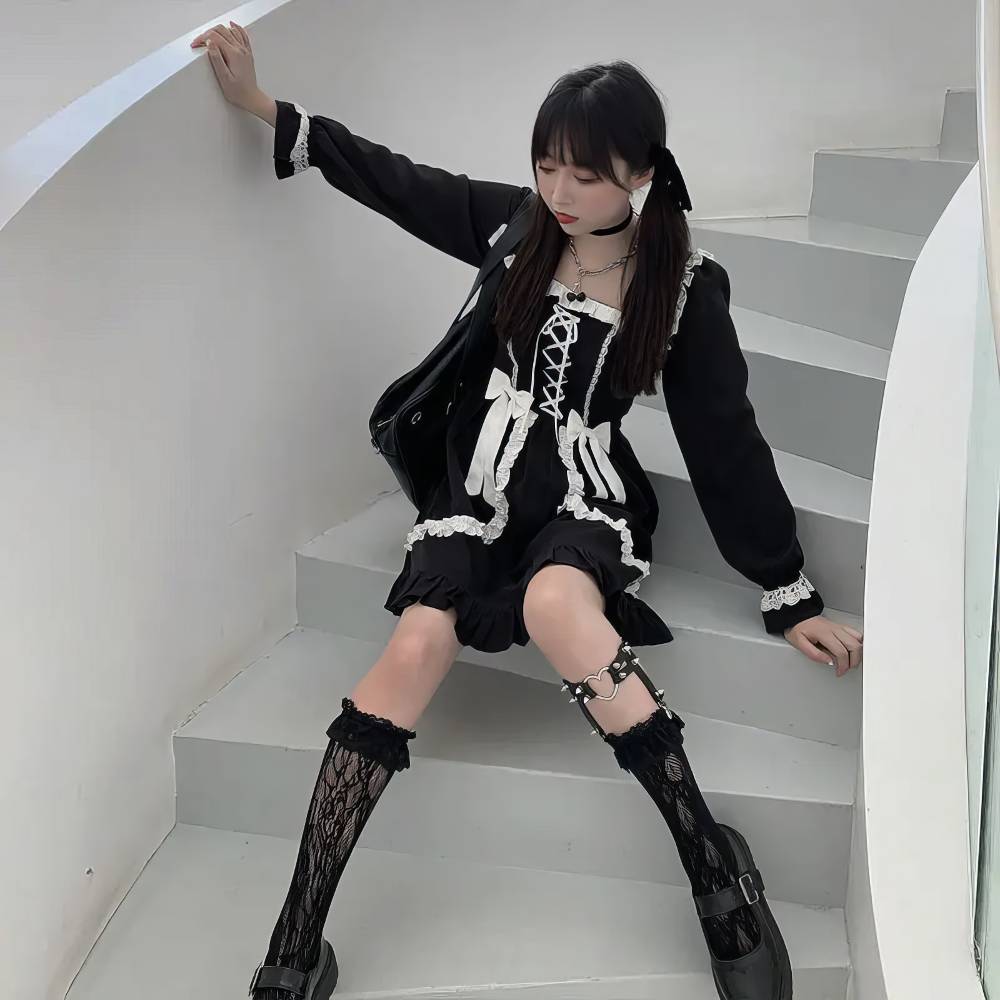 Robe gothique lolita noire SinisterSymphony avec dentelle blanche, corset lacé et volants, portée assise sur escalier