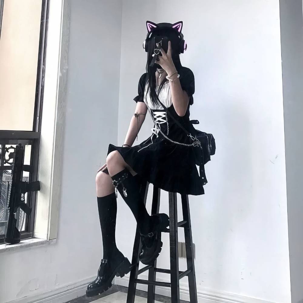 Robe style japonais gothique noire en velours avec corset blanc et jupe plissée portée assise sur un tabouret, look gothique chic avec accessoires noirs et casque à oreilles de chat