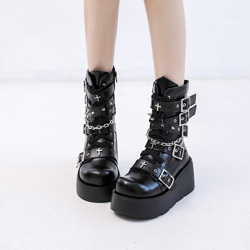 Bottes gothiques noires en cuir avec plateforme épaisse, ornées de croix métalliques, chaînes et boucles multiples, vue de face sur jambes