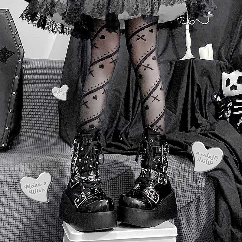 Bottes gothiques noires à plateforme épaisse avec croix et piques, détails en boucles métalliques, portées avec des collants noirs à motifs croix