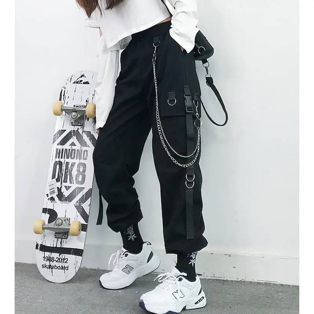 Pantalon femme gothique noir avec chaîne et sangles décoratives modèle RavenWhisper, porté avec baskets blanches et chaussettes noires