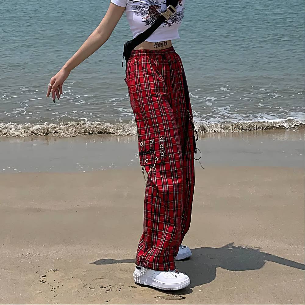 Pantalon gothique écossais PhantomPleat rouge à carreaux avec poches latérales et sangles porté de profil sur la plage