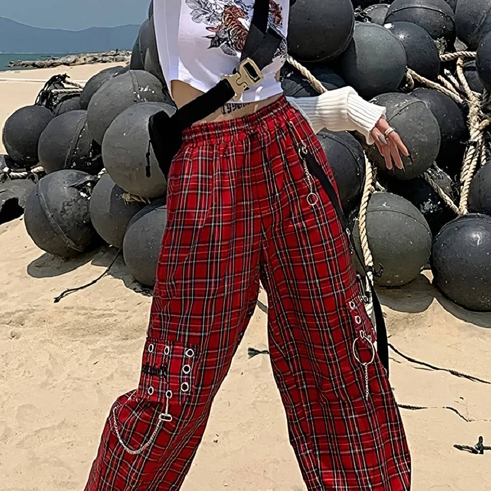Pantalon gothique écossais PhantomPleat rouge à carreaux avec chaînes et anneaux métalliques, porté en extérieur sur plage avec bouées noires en arrière-plan