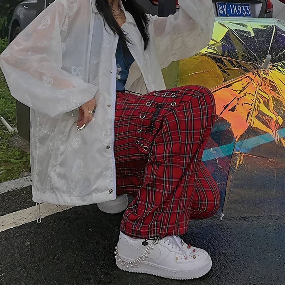 Pantalon gothique écossais PhantomPleat rouge à carreaux avec détails sangles métalliques porté avec veste blanche transparente et baskets blanches