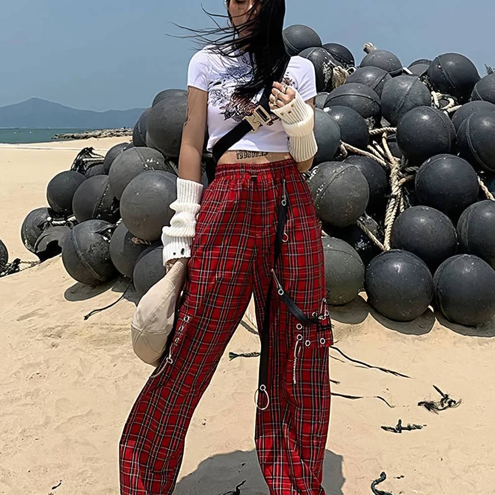 Pantalon Gothique Ecossais PhantomPleat rouge à carreaux noirs avec sangles et anneaux métalliques porté en extérieur sur plage
