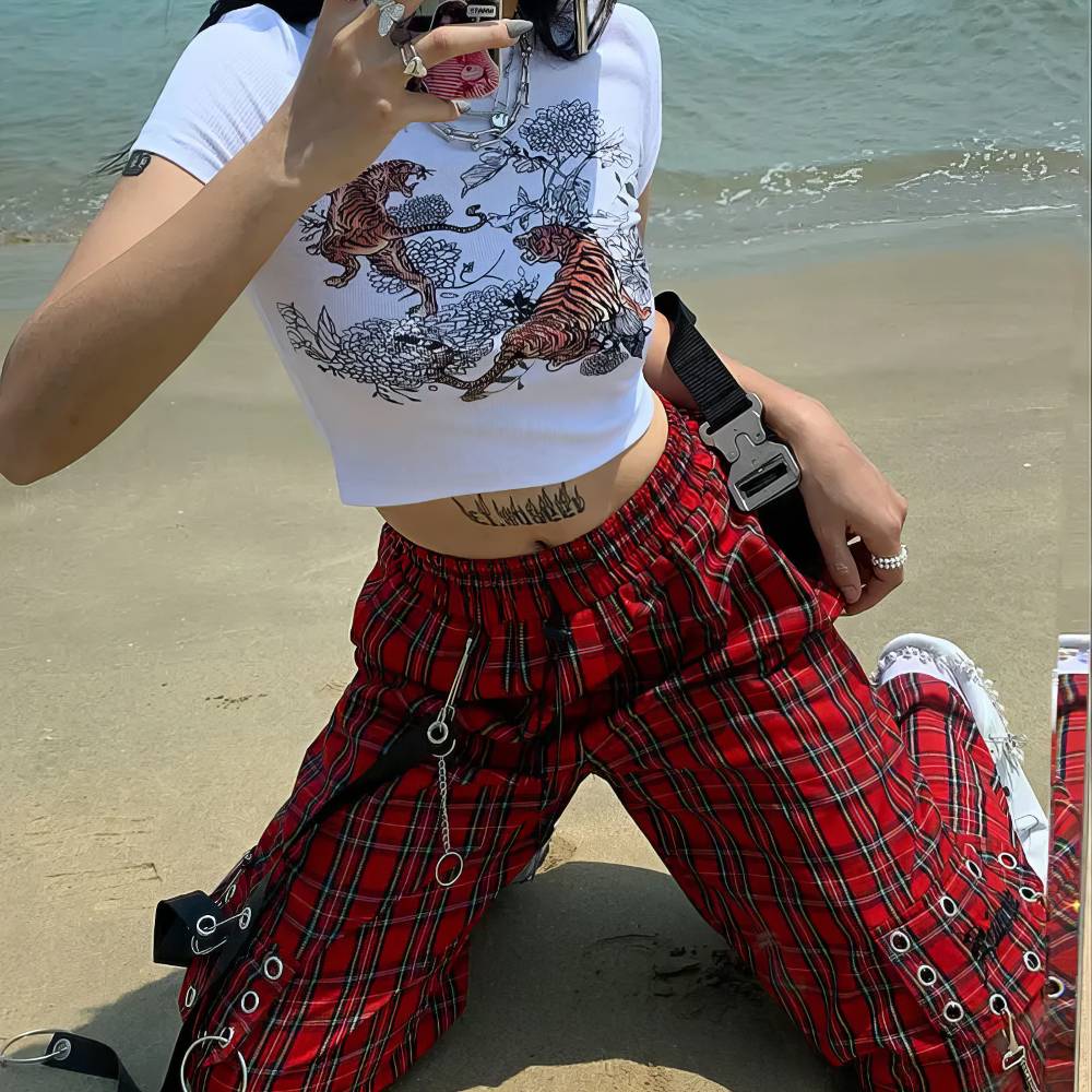 Pantalon gothique écossais PhantomPleat rouge à motifs tartan avec anneaux métalliques et sangles, porté sur une plage