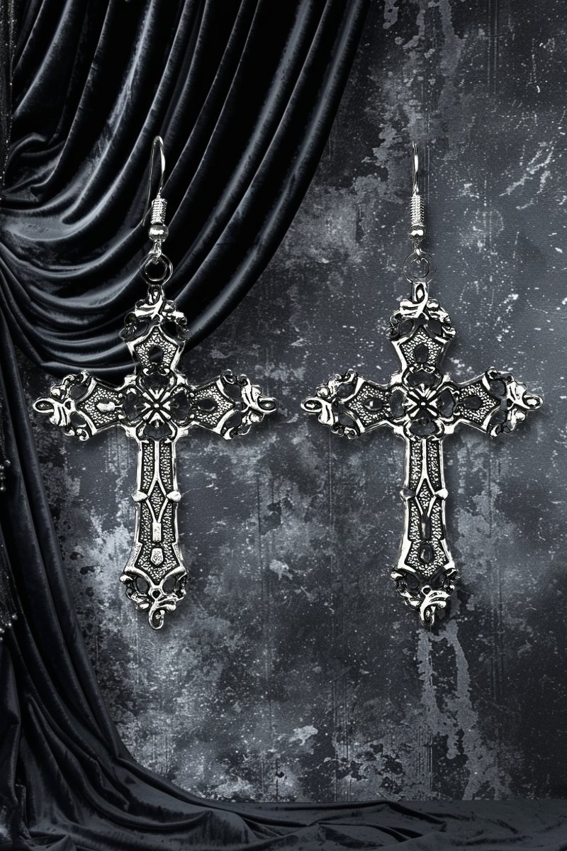 Boucle d'oreille croix gothique imposante en métal argenté avec détails ornementaux complexes sur fond noir texturé et velours noir