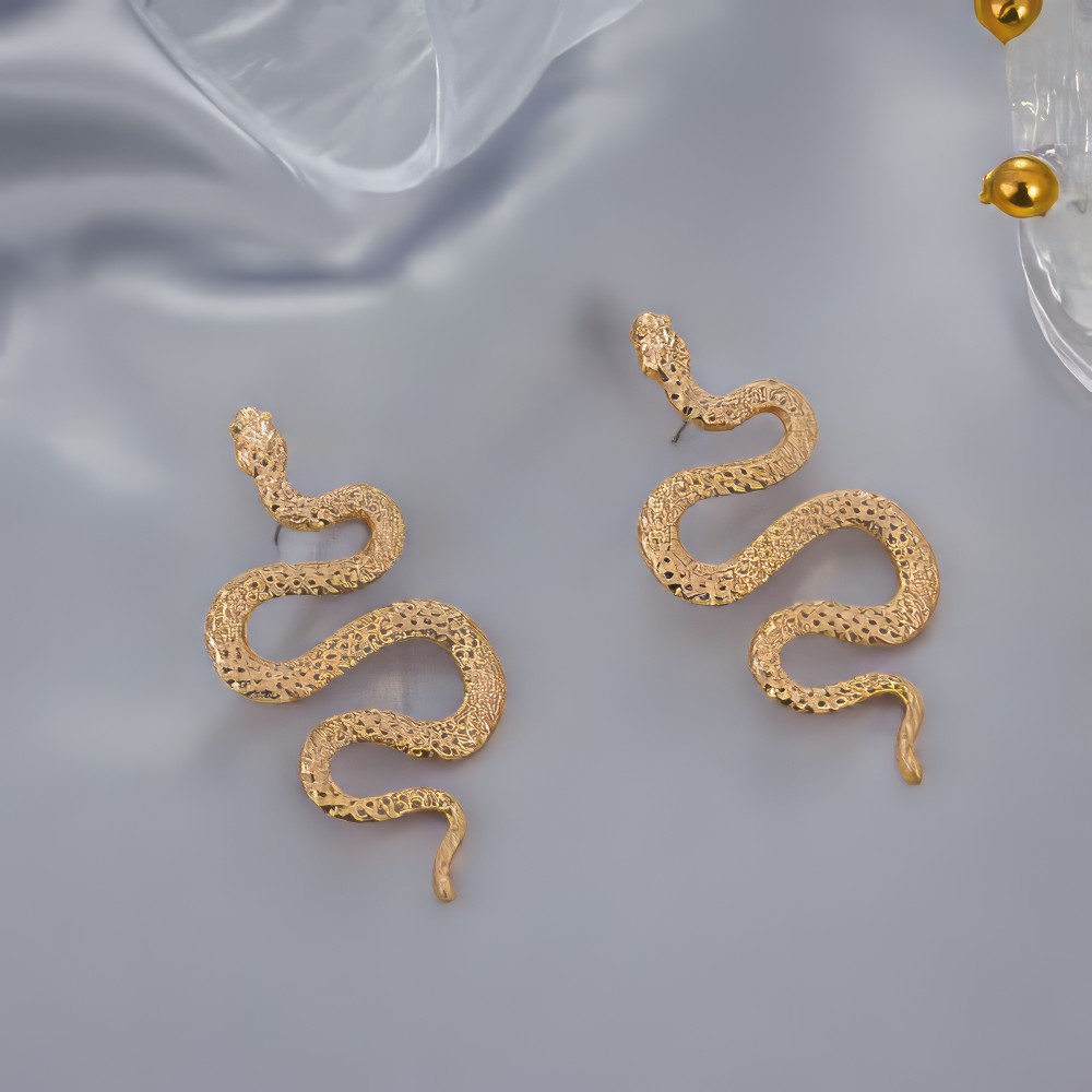Boucle d'oreille gothique serpent en S dorée avec texture écaillée modèle Ophidianeclipse sur fond gris satiné