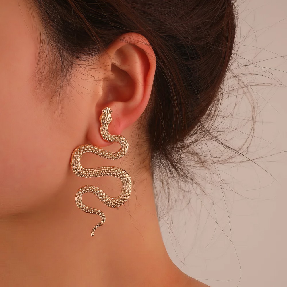 Boucle d'oreille gothique serpent en S dorée portée sur oreille, détail forme ondulée et texture écailles