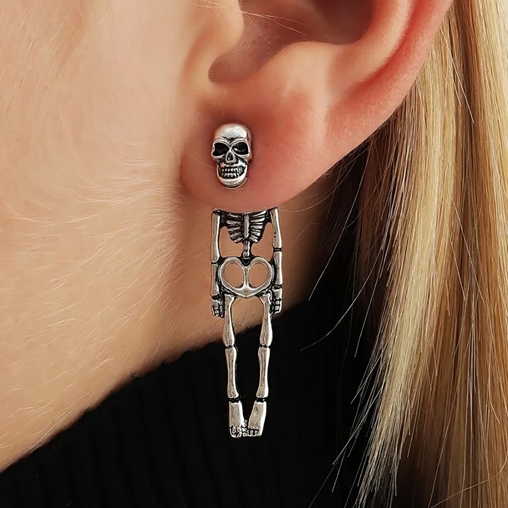 Boucle d'oreille gothique squelette allongé en métal argenté portée à l'oreille, détail du crâne et du corps squelettique suspendu