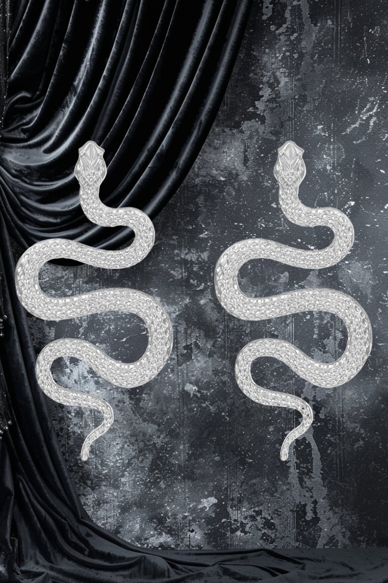Paire de boucles d'oreille gothique serpent en S couleur argentée avec texture détaillée, modèle Ophidianeclipse, posées sur fond noir velours et surface grise texturée