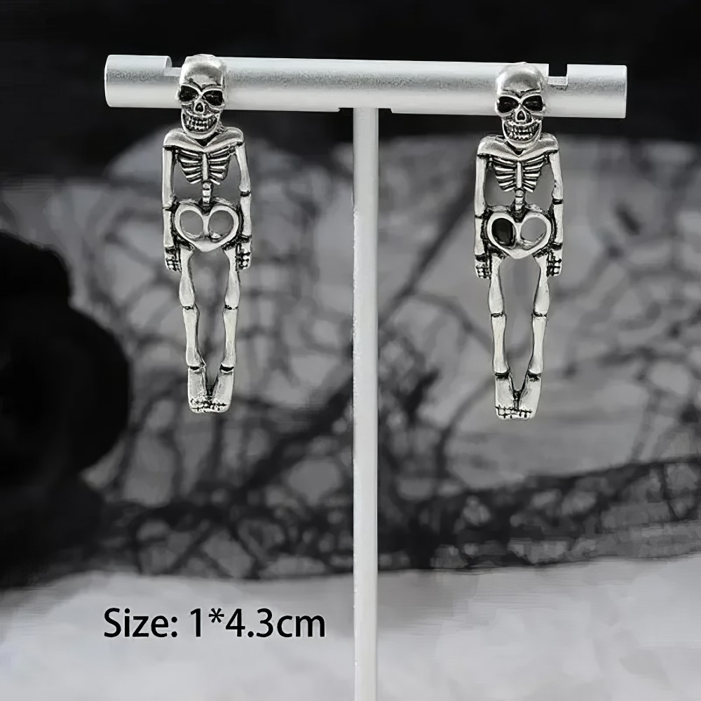 Boucles d'oreilles gothiques en métal argenté représentant des squelettes allongés avec un cœur au niveau du bassin, modèle Skeletonsoul, vue frontale sur support blanc