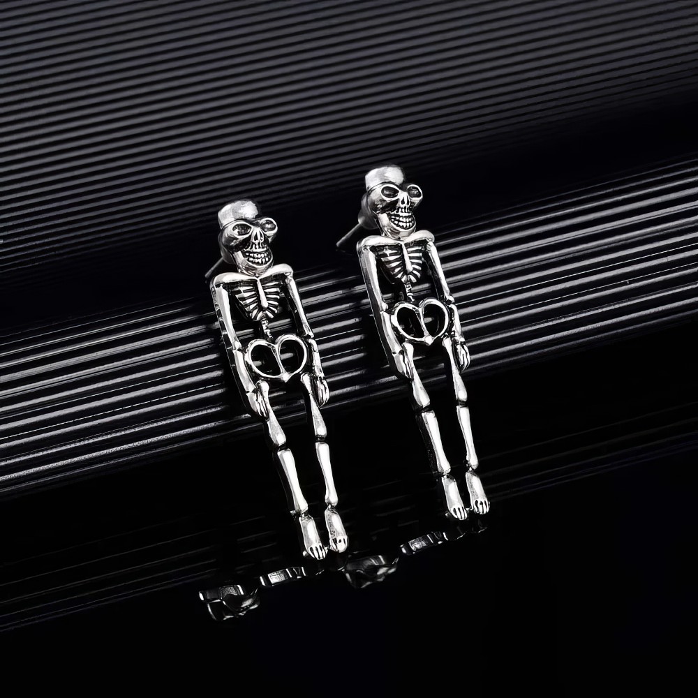 Boucles d'oreilles gothiques squelette allongé en métal argenté avec détails osseux visibles, posées sur surface noire brillante