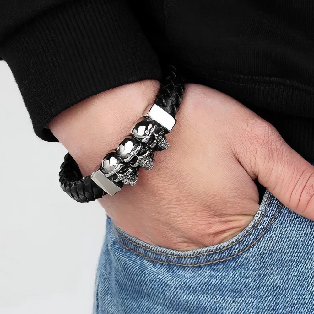 Bracelet gothique triple tête de mort en cuir tressé noir avec détails métalliques argentés porté au poignet
