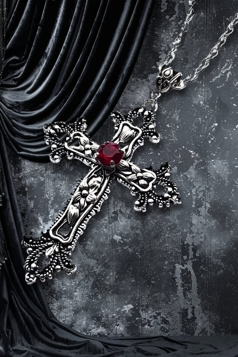Collier croix gothique en métal argenté avec pierre rouge centrale CrimsonCross sur fond sombre avec tissu noir drapé