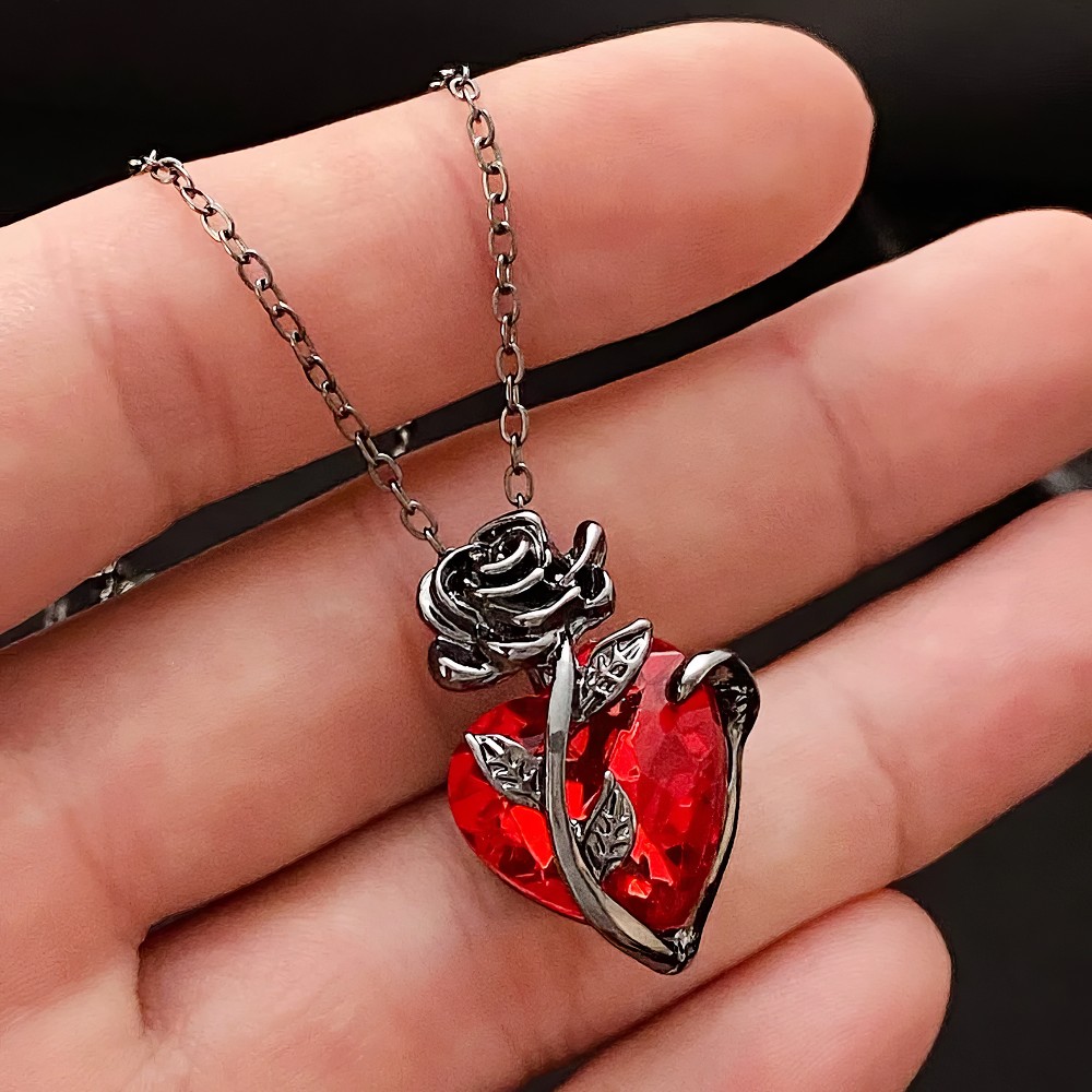 Collier gothique cœur rouge en cristal avec motif rose en métal argenté tenu dans une main