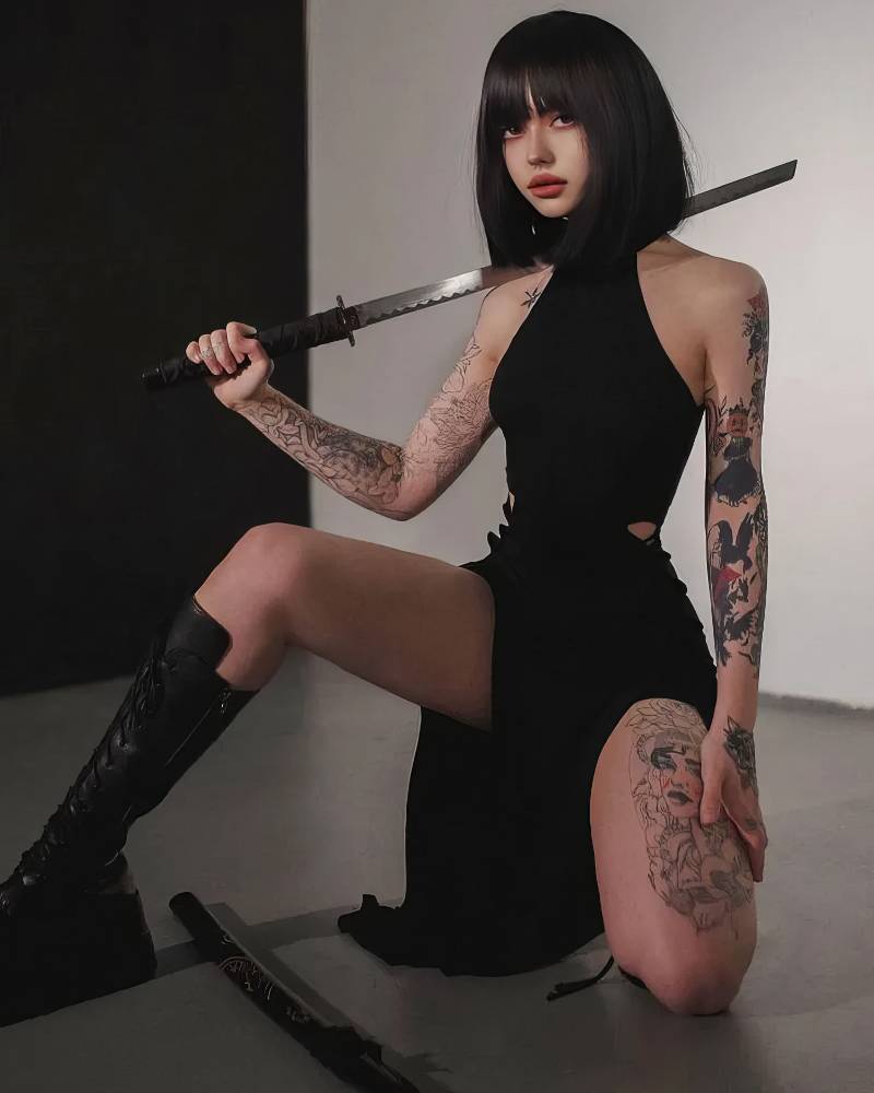 Robe gothique fendue sexy noire BlackBanshee en tissu uni avec col montant portée par un modèle assis, montrant la fente haute et les détails du tissu