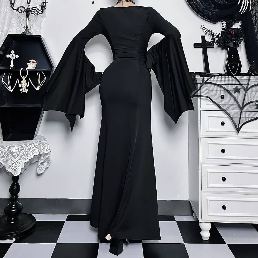 Robe gothique Morticia Addams noire en tissu fluide avec manches longues évasées vue de dos dans un décor sombre gothique